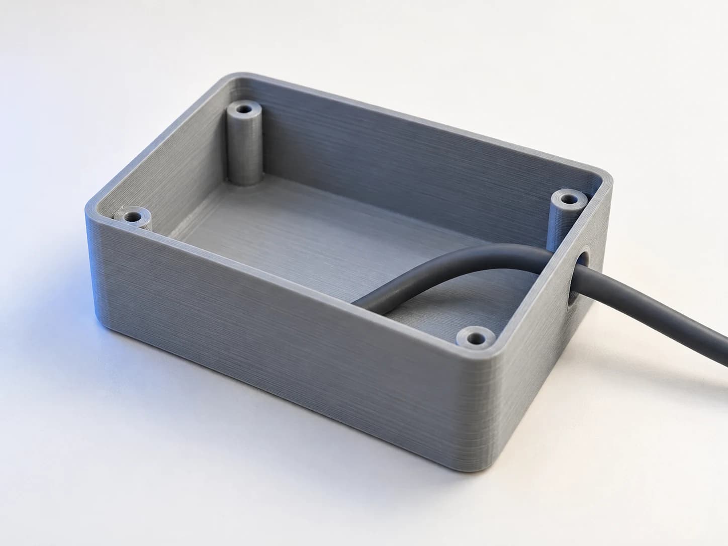 An open grey printed enclosure with a single cable routed through a side cutout.