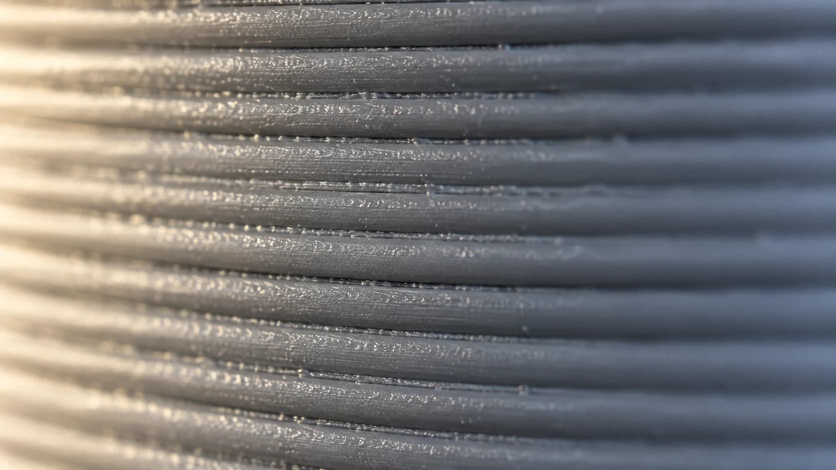 An extreme close view of even horizontal layer lines on a grey printed wall.