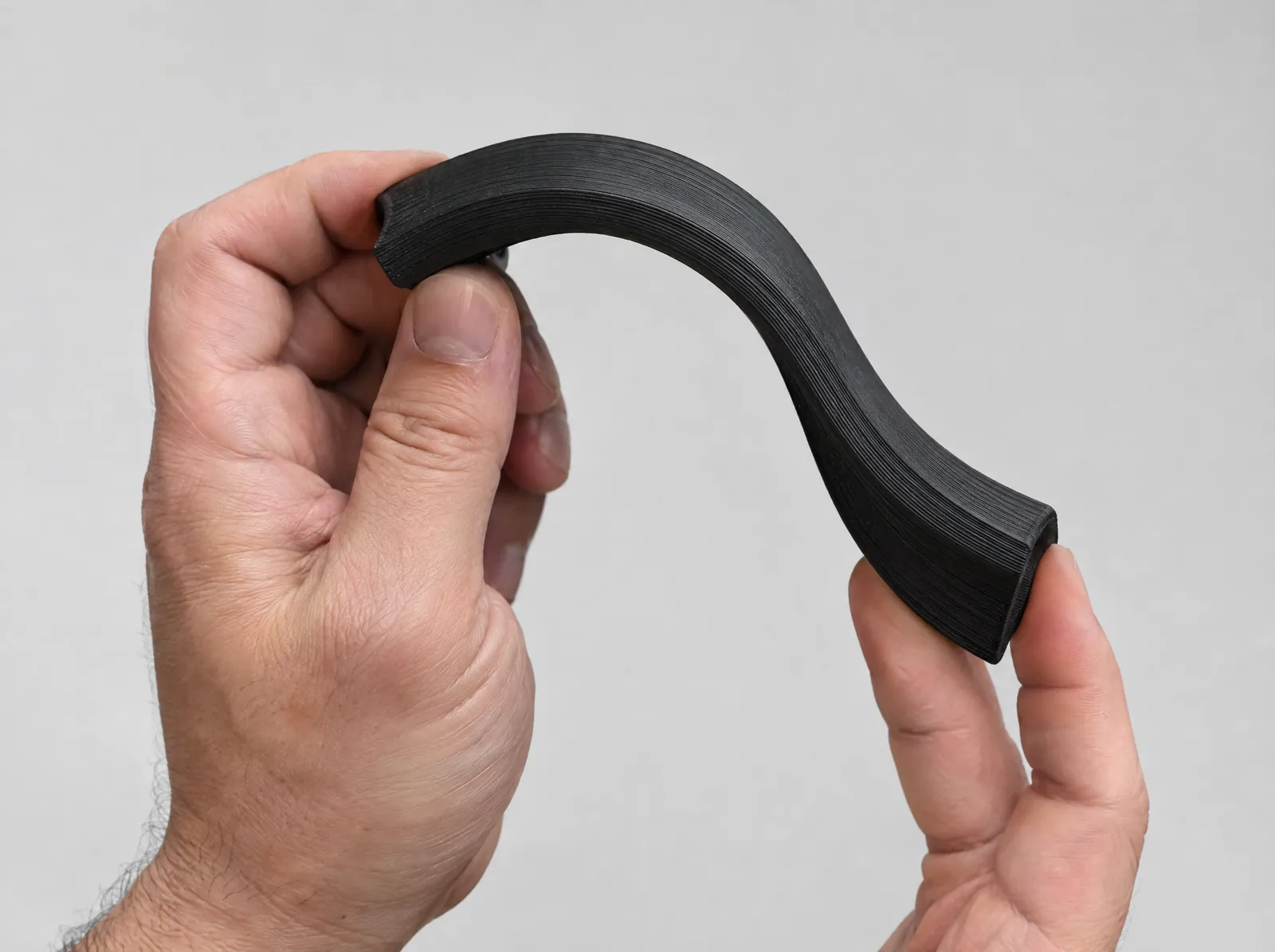 Two hands bending a flexible black printed strip into an S shape.
